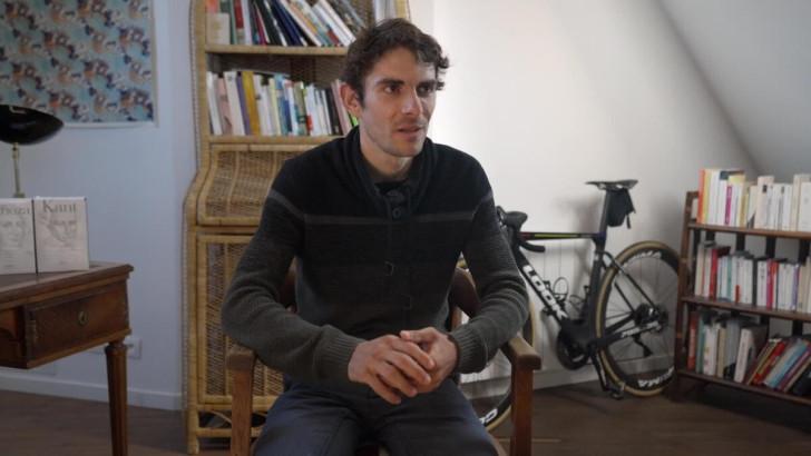 Le cycliste Guillaume Martin assis chez lui (on aperçoit derrière lui un vélo de course)